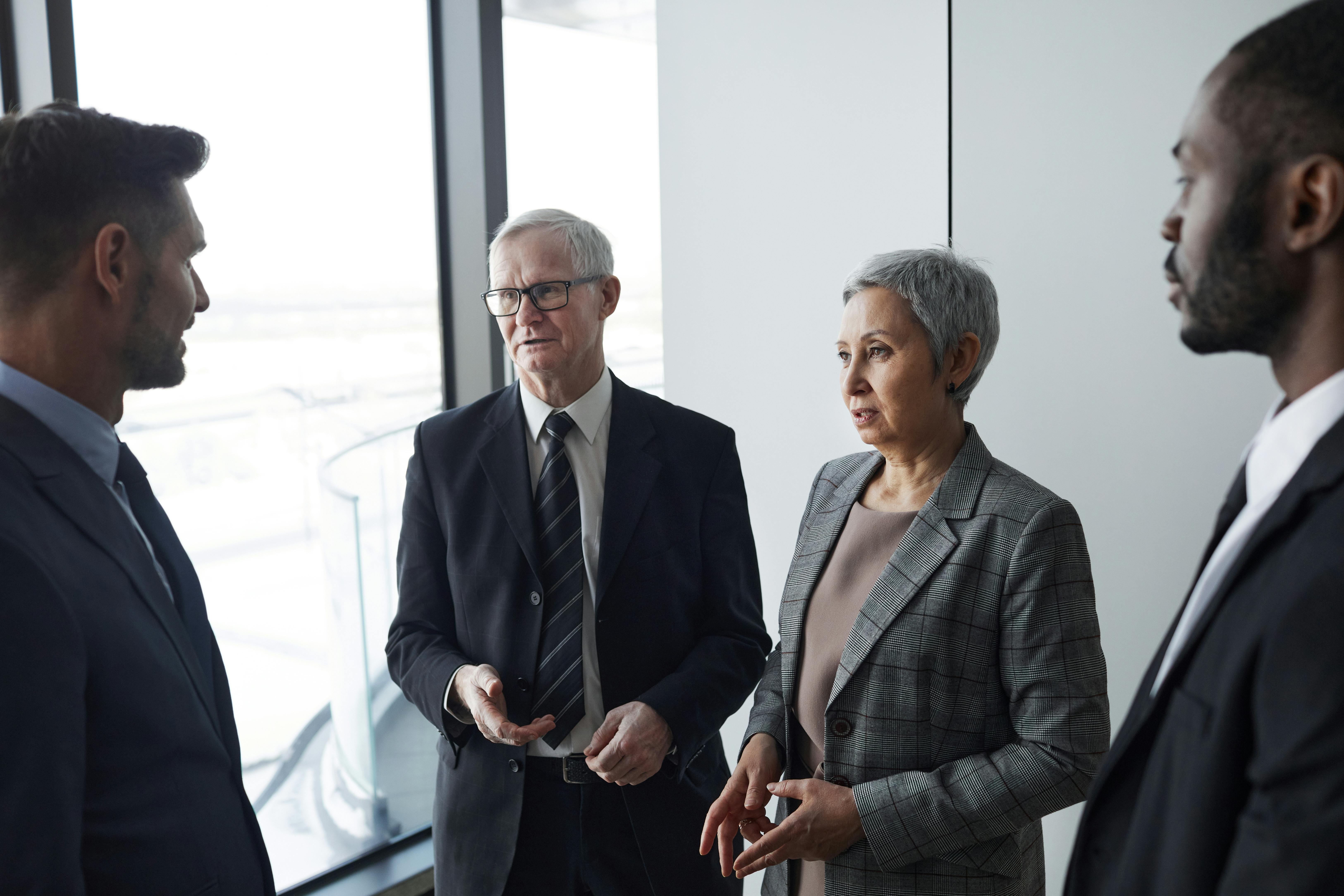 An elderly man and woman talking to two men, all dressed in business attire