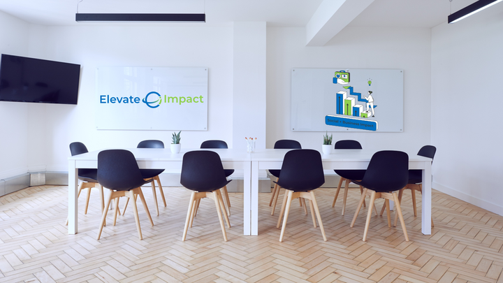 Empty chairs around a table in a bright room, with a canvas on the wall that says 'Elevate Impact'